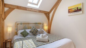 Une chambre avec un plafond en bois, un lit avec une literie à motifs, une tête de lit ornée de motifs floraux et un tableau accroché au mur.