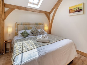 Une chambre avec un plafond en bois, un lit avec une literie à motifs, une tête de lit ornée de motifs floraux et un tableau accroché au mur.