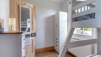 A bedroom with a bunk bed, a wooden wardrobe, a mirror, and a window.