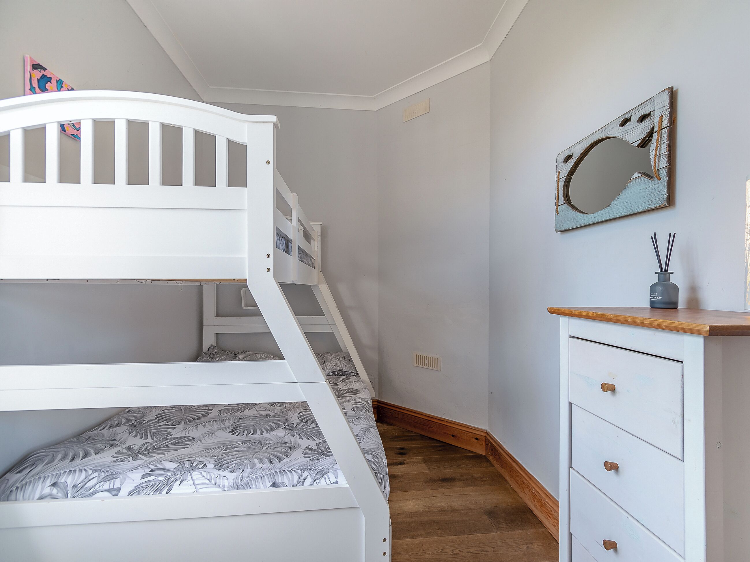 Ein Etagenbett mit Holzleiter, eine weiße Kommode mit Schubladen und ein Spiegel an der Wand.