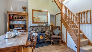 Una sala acogedora con chimenea, muebles de madera, una estantería y una escalera.