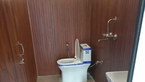 Ein kleines Badezimmer mit Toilette, einem roten Hocker und einem blauen Eimer.