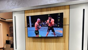 Een aan de muur bevestigde televisie toont een UFC-gevecht, een houten paneel en een keuken met apparatuur.