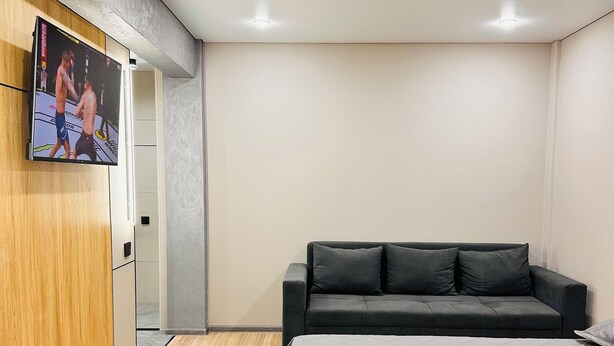 Een moderne slaapkamer met een bed, een aan een houten kast bevestigde televisie, een donkere bank en een houten vloer.
