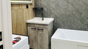 Een moderne badkamer met een marmeren wand, een houten wastafelmeubel, een witte wastafel en een bad.