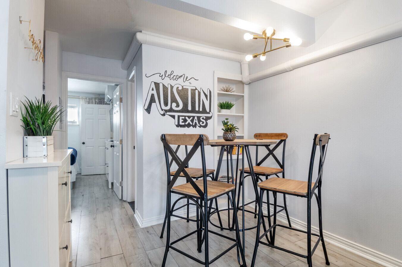 A modern kitchen with a 'Welcome to Austin, Texas' sign, wooden chairs, and a pendant light.
