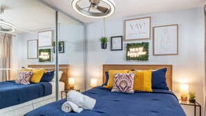 Moderni hotellihuone, jossa on suuri sänky, yöpöydät, kattotuuletin ja koristeellinen seinätaide.
