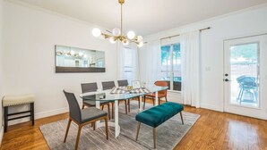 Een eetruimte met een glazen tafel, stoelen, een bank, een kroonluchter en uitzicht door een deur.