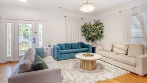 Een ruime woonkamer met een blauwe bank, een beige bank en een witte salontafel.