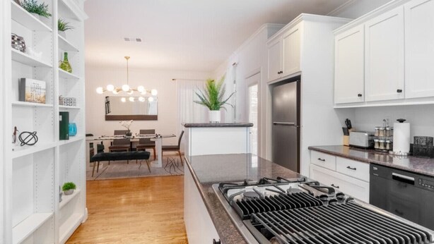 Een moderne keuken met witte kastjes, een centraal eiland met een kookplaat en een eethoek met een kroonluchter.