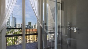 A modern bathroom with a glass shower door, a visible cityscape view, and a balcony with a railing. - Repubblica City View by Interhome (Milan)