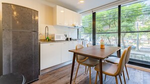 A modern kitchen with white cabinets, a wooden dining table, and a view of the outdoors through large windows. - VH | Condesa 2 bedroom apartment | 245 (Ciudad de México)