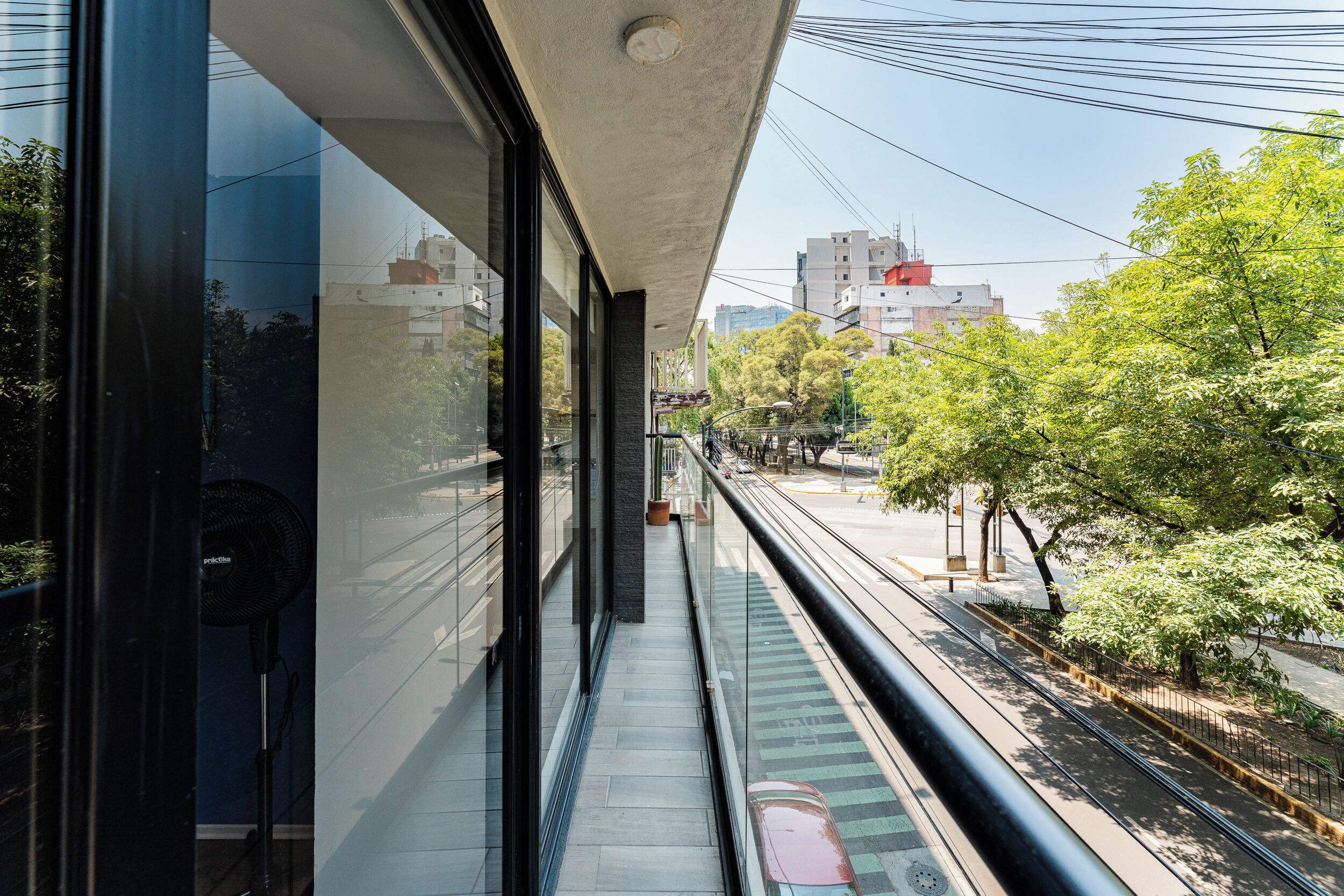 A modern building with large glass windows, a balcony with a metal railing, and a view of a street with trees and buildings.