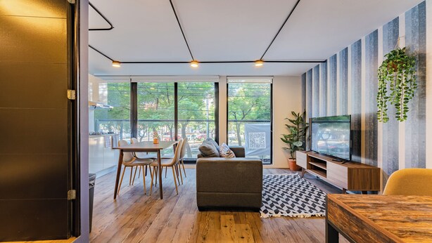 A modern living room with a sofa, dining table, and TV. Large windows provide a view of the outdoors. - VH | Condesa 2 bedroom apartment | 245 (Ciudad de México)