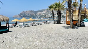 Une plage avec des parasols, des chaises longues et des palmiers.