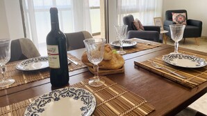 Une table à manger dressée avec des assiettes, des verres et une bouteille de vin, avec un canapé et une plante en arrière-plan.