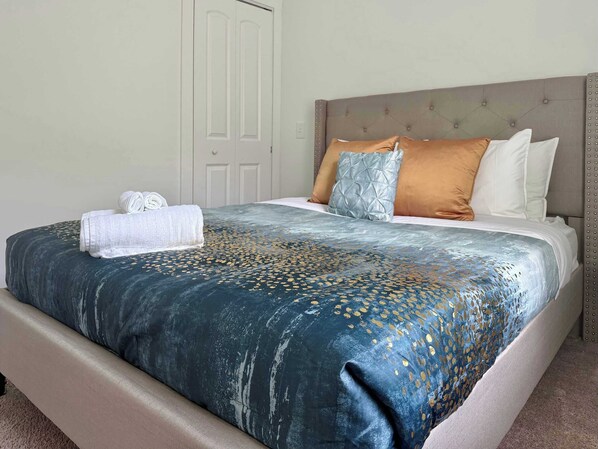 A neatly made bed with a patterned bedspread, pillows, and a rolled white towel.