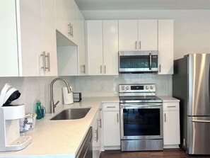 A modern kitchen with white cabinets, stainless steel appliances, a microwave, oven, and a refrigerator.