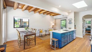 Une cuisine spacieuse avec un plafond en bois, un îlot central bleu et un coin repas doté de chaises en bois.