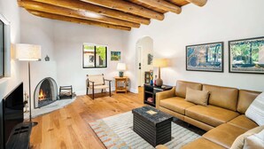 Un salon avec une cheminée, des poutres apparentes, un canapé, une table basse et des œuvres d’art encadr ées accrochées au mur.