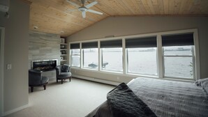 A bedroom with a large window overlooking a body of water, a ceiling fan, and a built-in entertainment unit. - Park Point Oasis | On Lake Superior | Duluth (Duluth)