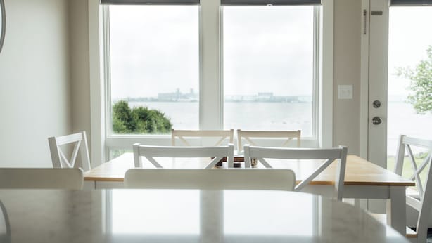 A dining area with a table and chairs, large windows with a view of a body of water and a distant cityscape. - Park Point Oasis | On Lake Superior | Duluth (Duluth)