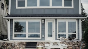 A two-story house with a covered patio area featuring a picnic table and a trash can. - Park Point Oasis | On Lake Superior | Duluth (Duluth)
