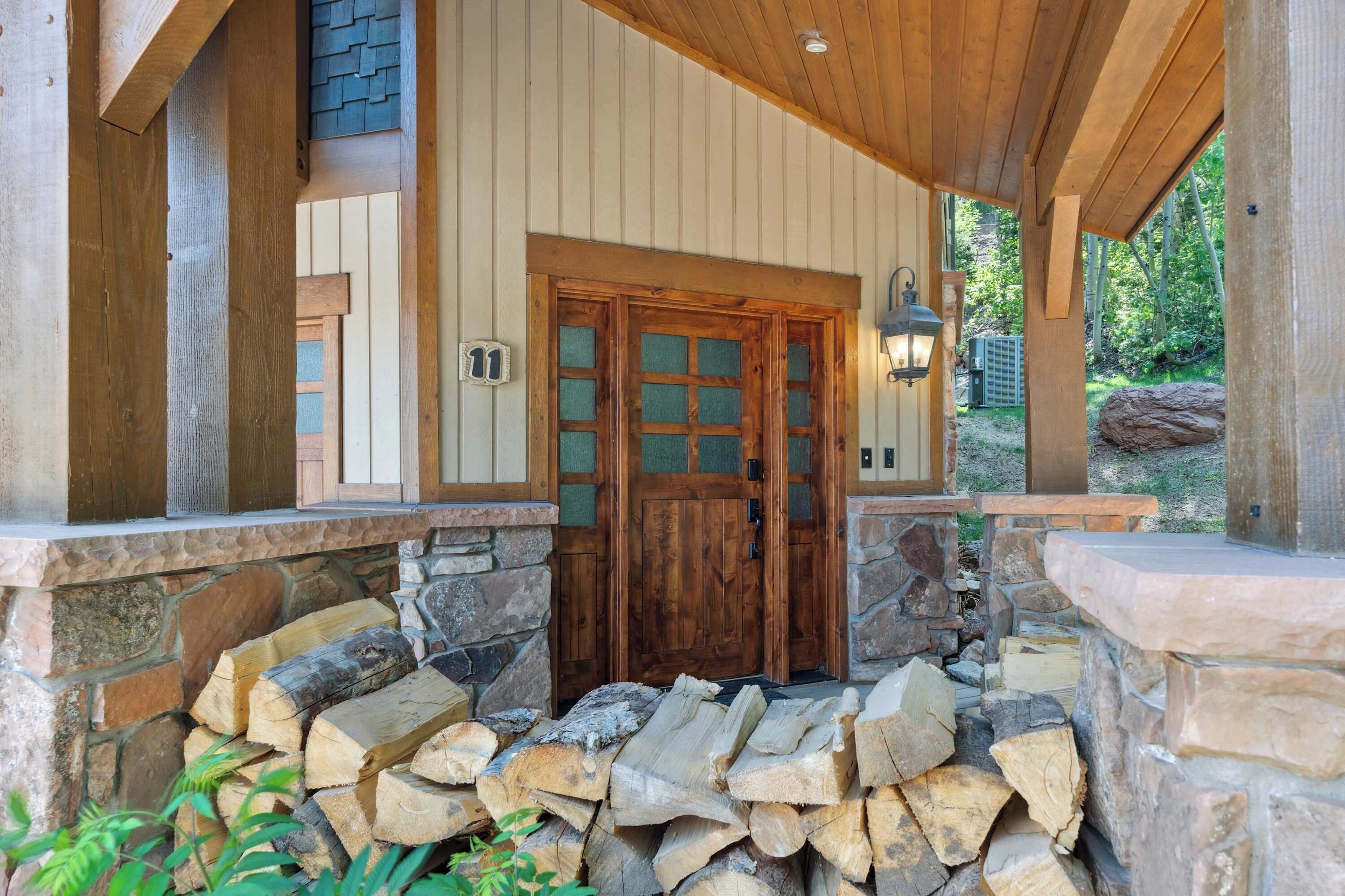 A wooden cabin entrance with a stone foundation, a wooden door with glass panels, and a stone fireplace.