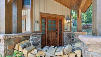 A wooden cabin entrance with a stone foundation, a wooden door with glass panels, and a stone fireplace.