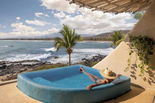 Una persona relajándose en un jacuzzi con vista al océano y a las montañas.
