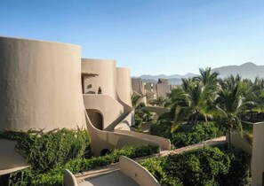 Un resort con arquitectura moderna, palmeras y montañas al fondo.