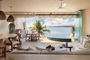 Una habitación con vista al océano, una mesa redonda, sillas, un sofá y una pequeña piscina.