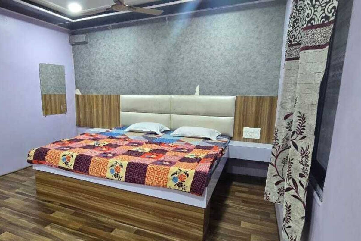 A bedroom with a wooden floor, a bed with a colorful quilt, a headboard, a nightstand, and a wall-mounted air conditioner.