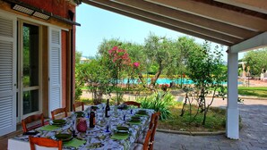 Un espacio de comedor al aire libre con una mesa preparada para cuatro personas, rodeada de sillas y vistas a una piscina y vegetación.