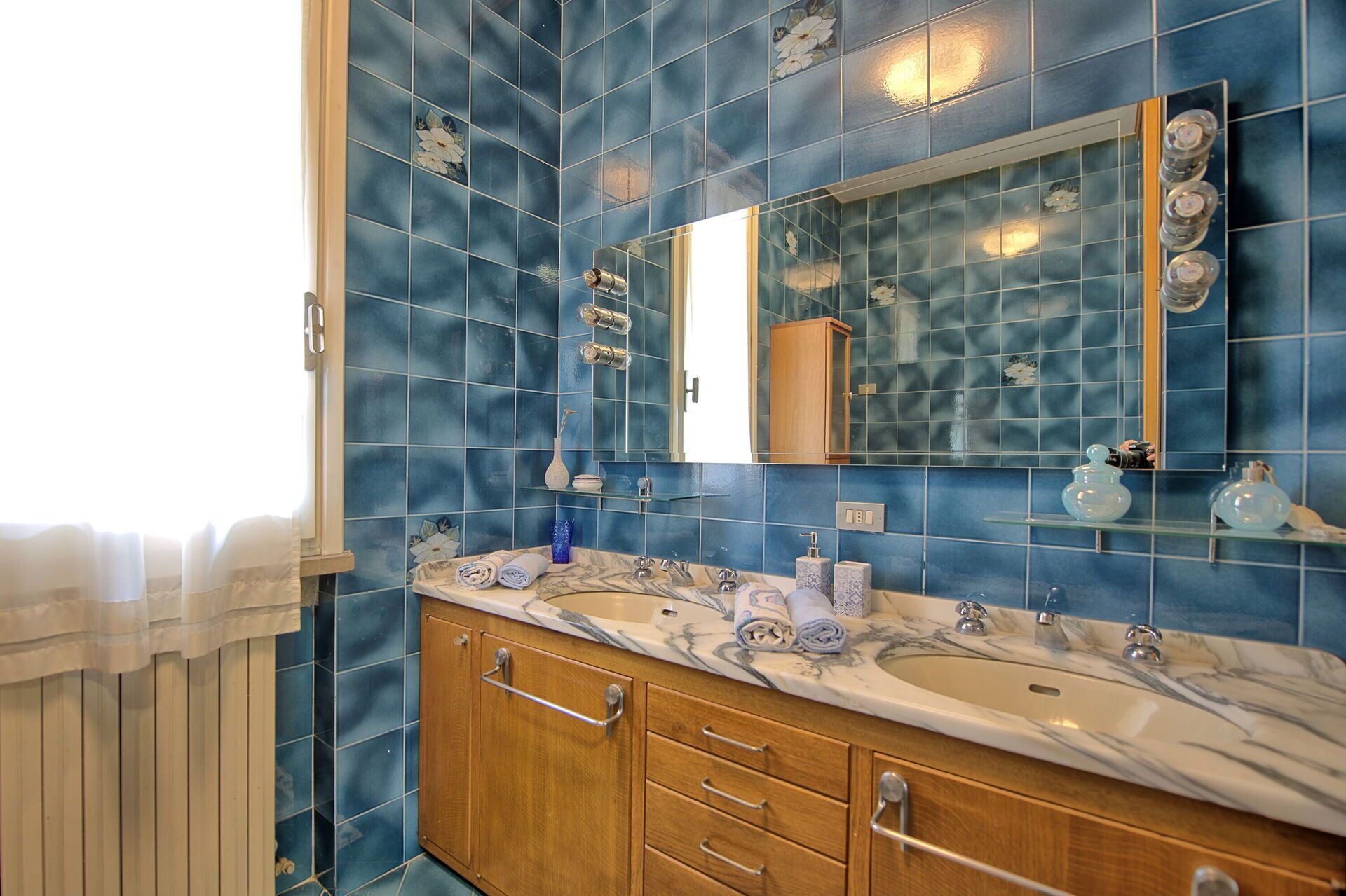 A bathroom with blue tiles, a marble sink, and wooden cabinets.