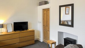 A living room with a television on a wooden dresser, a small table, a brown leather sofa, and a fireplace. - Hidden Treasure-UK48779 (Whitby)