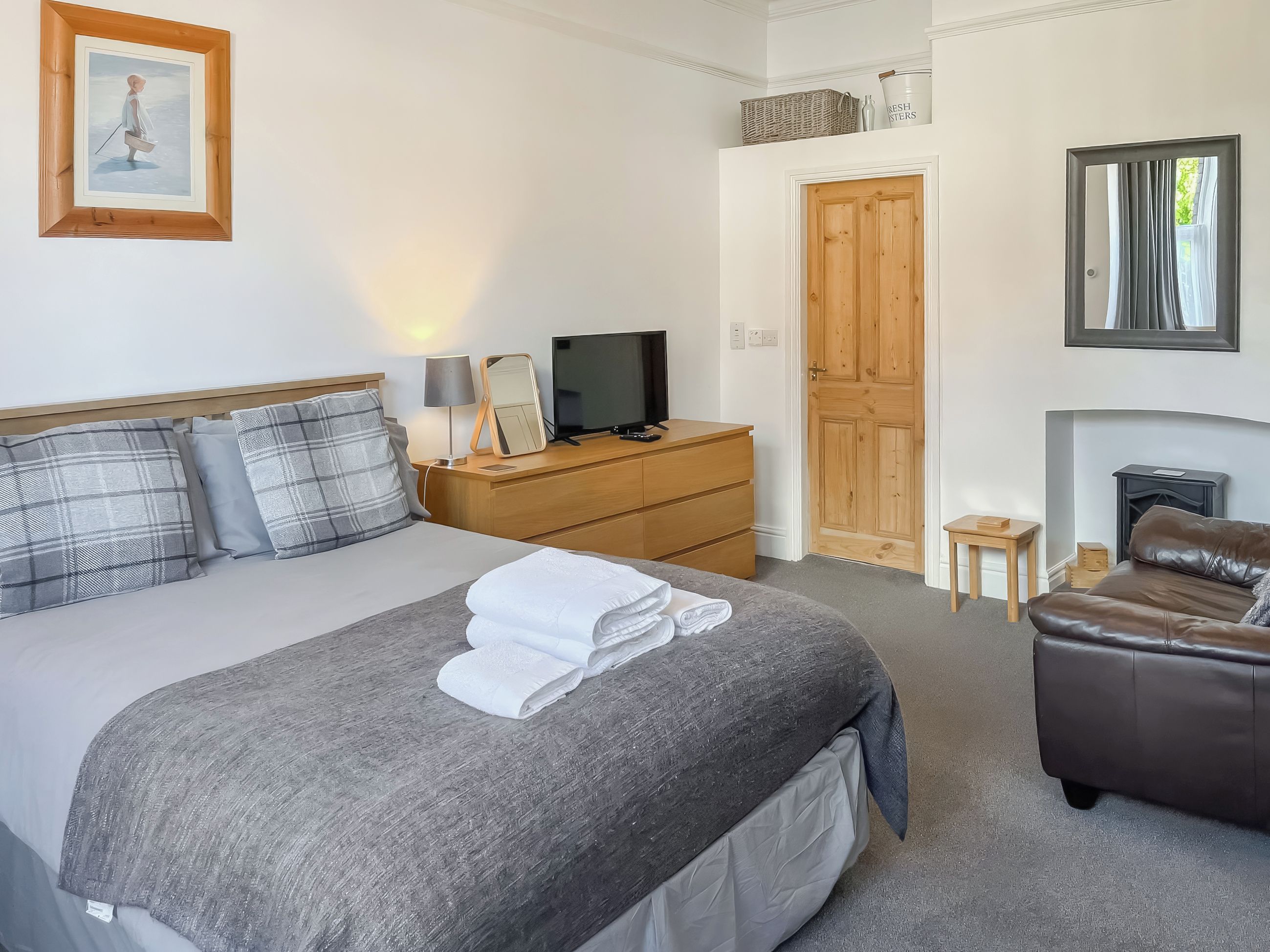 A hotel room with a bed, a television, a dresser, a mirror, a fireplace, and a leather sofa.