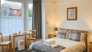 A hotel room with a bed, a desk, a chair, a radiator, and a window with curtains. - Hidden Treasure-UK48779 (Whitby)