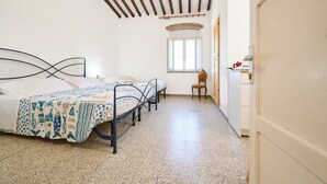 Une chambre avec un lit, une chaise, une fenêtre et un coin cuisine.