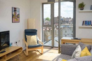 Una sala de estar moderna con un ventanal grande, un sillón azul, un sofá gris, una mesa de centro de madera y una estantería.