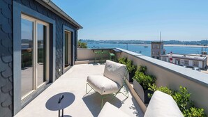 A balcony with a view of the sea, a chair, a small table, and a building with a tower in the background. - Oceanfront Villa, Near Porto Historical Centre (Porto)