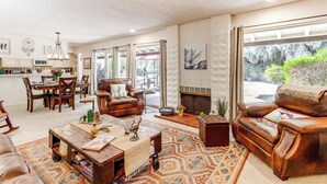 Ein geräumiges Wohnzimmer mit Kamin, Ledersofas, einem Couchtisch und einem Essbereich mit Stühlen und Tisch.