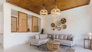 A modern living room with a white sofa, a round coffee table, and a ceiling with wooden beams.