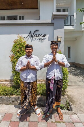 Two individuals standing in front of a building with a sign that reads "Namo Villa."