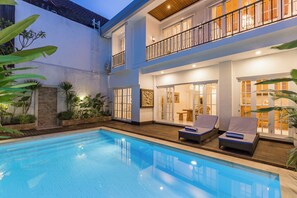 A two-story building with a swimming pool, outdoor seating, and a well-lit balcony.