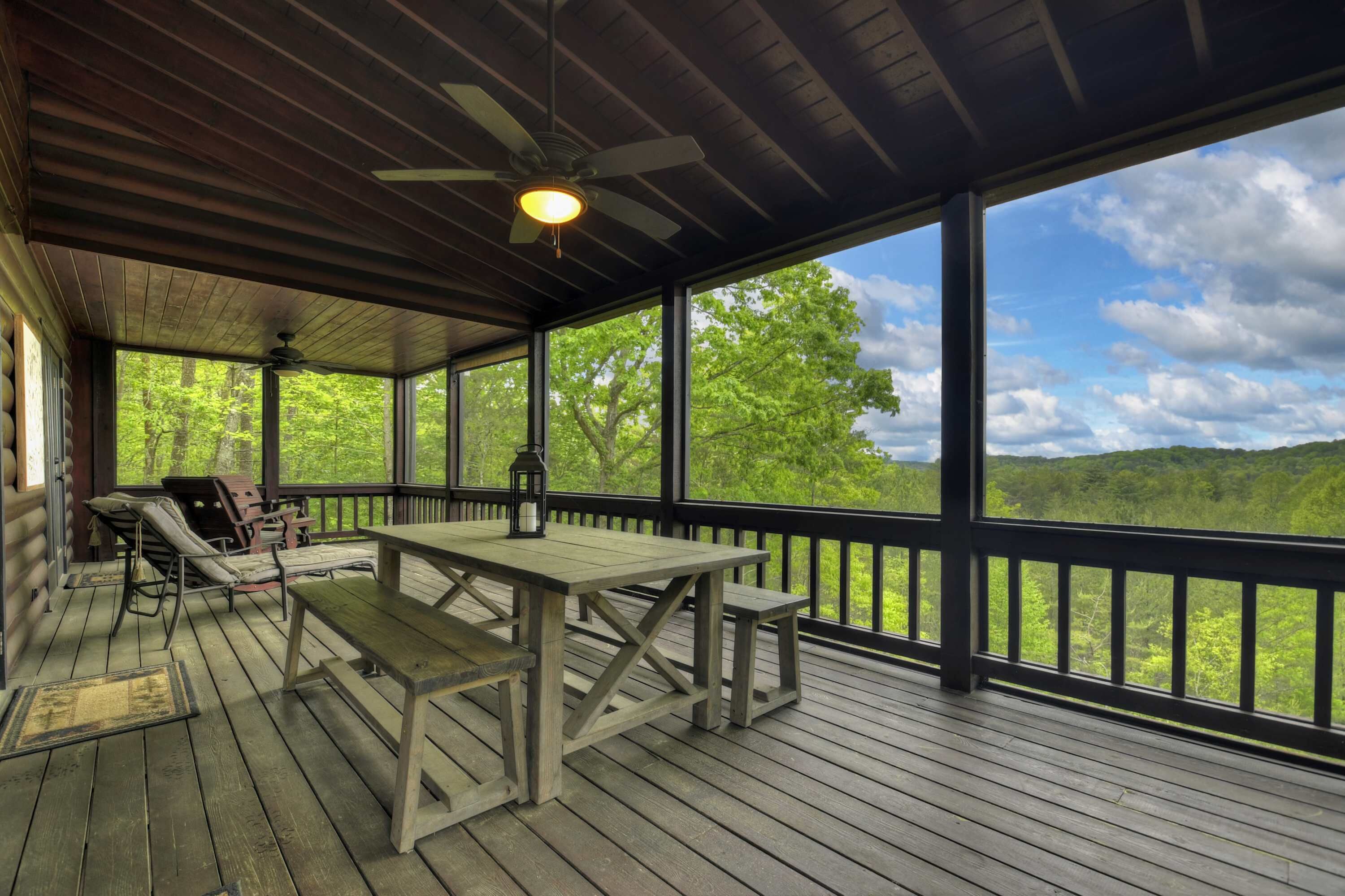 A covered outdoor deck with a table and benches, large windows offering a view of a forested landscape.