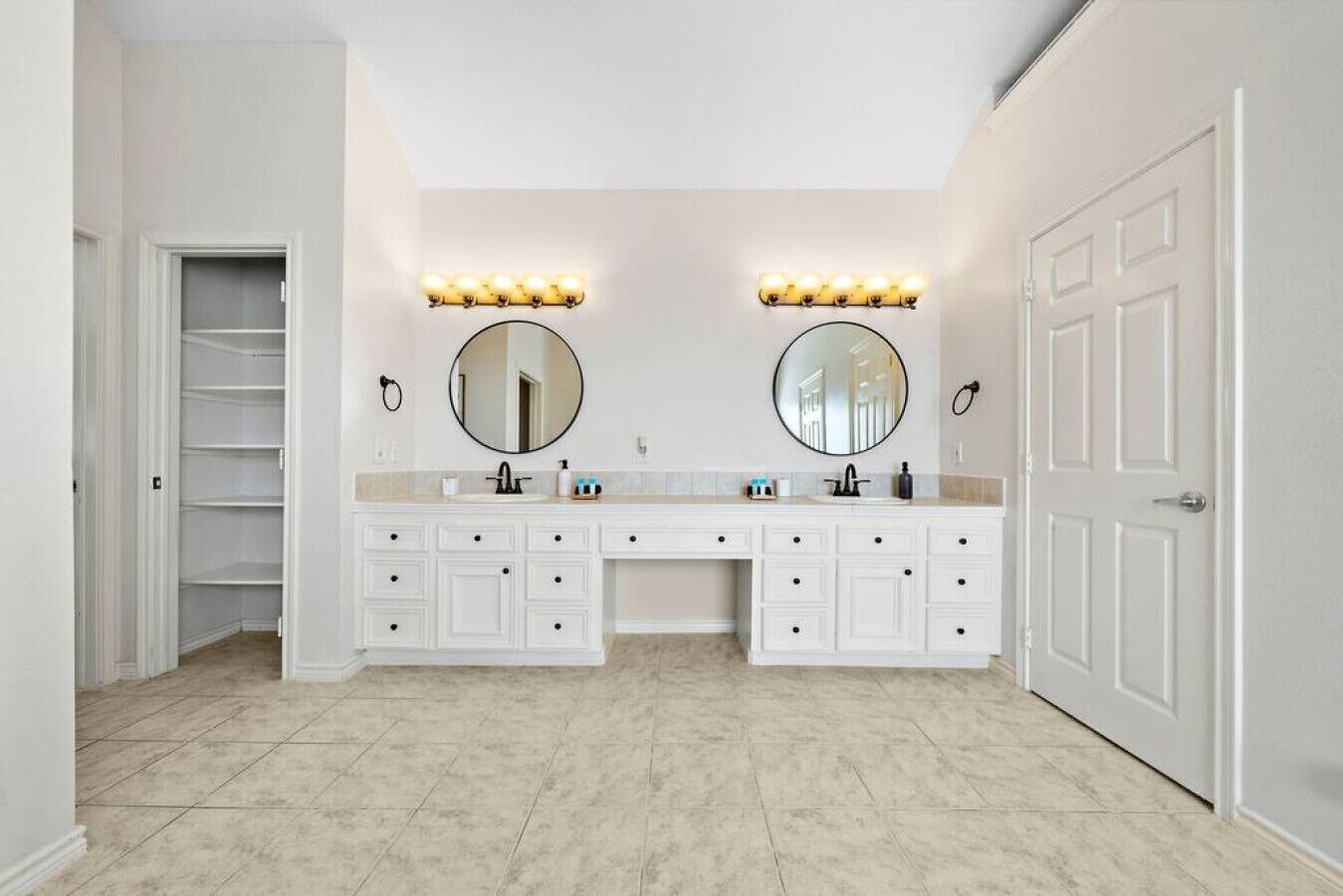 A bathroom with two sinks, a walk-in closet, and a door.