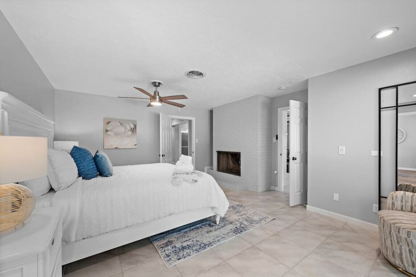 A bedroom with a bed, a ceiling fan, a fireplace, and a door leading to another room.