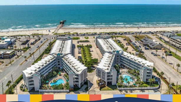A coastal hotel with multiple buildings, a parking lot, and a beach view. - Cute condo on Seawall across from beach (Galveston)