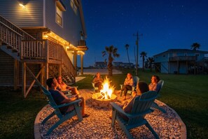 A group of people seated around a fire pit in a backyard with a house in the background.